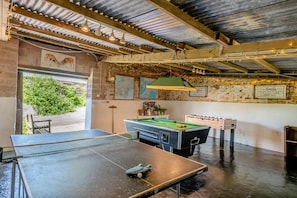A billiards table, foosball table, and a pool table in a room with a rustic ceiling and exposed beams.