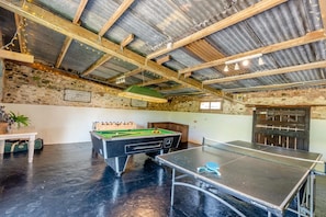 Une table de billard, une table de pool et une table de baby-foot se trouvent dans une pièce rustique aux poutres apparentes et aux murs en pierre.