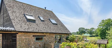 A stone house with a sloped roof, a wooden door, and a small garden with potted plants.