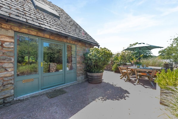 Ein Steinhaus mit einer grünen Tür, einer Terrasse mit Tisch und Stühlen und einem großen Topfpflanzen.