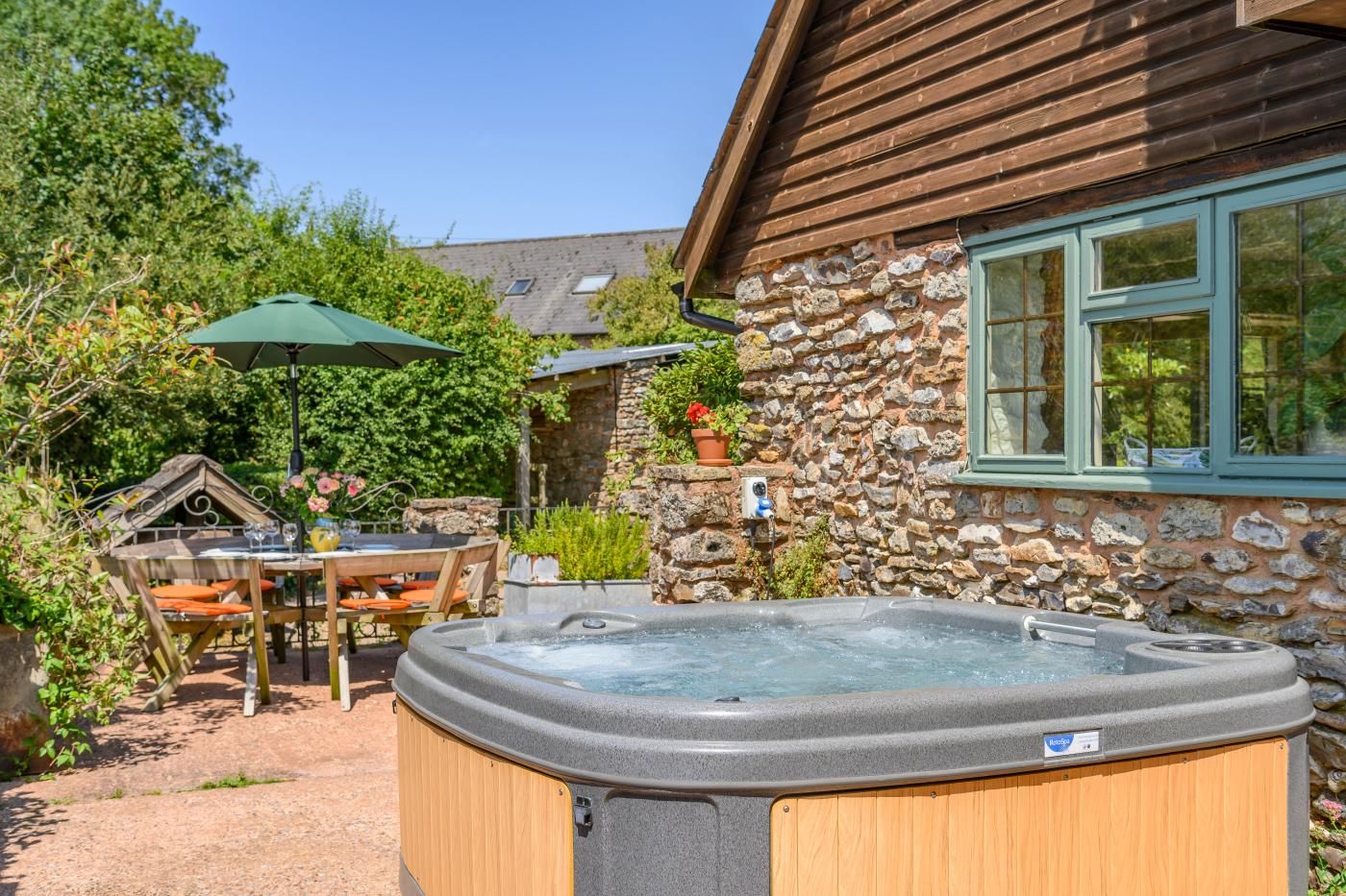 Tinaco en un jardín con pared de piedra, terraza de madera y mobiliario exterior.