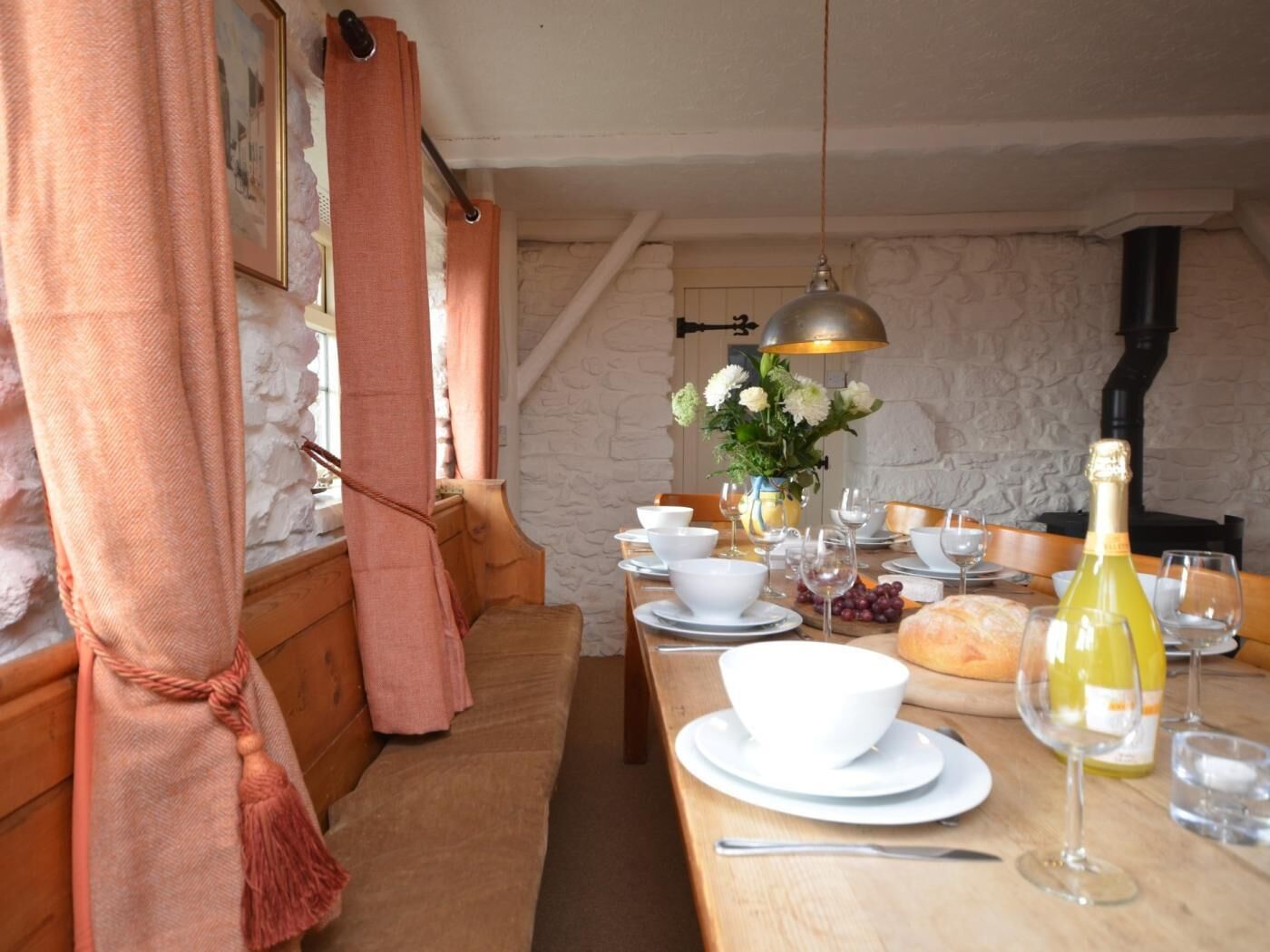 Un coin repas avec une table en bois dressée pour le repas, un lustre et un mur en pierre en arrière-plan.