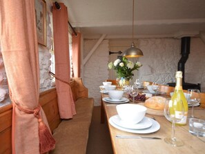 A dining area with a wooden table set for a meal, a chandelier, and a stone wall in the background. - 4 Bed in Honiton (oc-41045) (Sheldon)