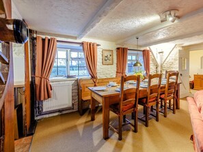 A dining area with a wooden table and chairs, a radiator, and a window with curtains. - 4 Bed in Honiton (oc-41045) (Sheldon)