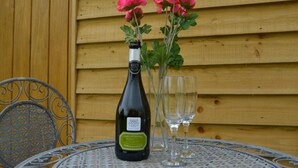 A bottle of wine, two glasses, and pink flowers on a table against a wooden wall. - 1 Bed in Axminster (oc-36491) (Dalwood)