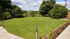 A well-maintained lawn with a stone border, surrounded by dense foliage and a clear sky. - 1 Bed in Axminster (oc-36491) (Dalwood)