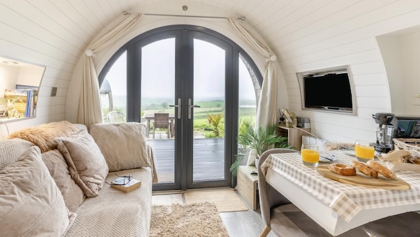 A cozy room with a large arched window, a sofa, a dining table with breakfast items, and a TV.