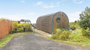 A wooden structure with a circular window, surrounded by a gravel path and greenery.