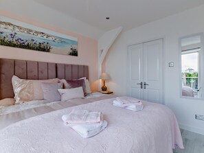 Une chambre à coucher avec un grand lit, une tête de lit, un tableau au-dessus du lit, une table de chevet avec une lampe et une fenêtre donnant sur un beau paysage.