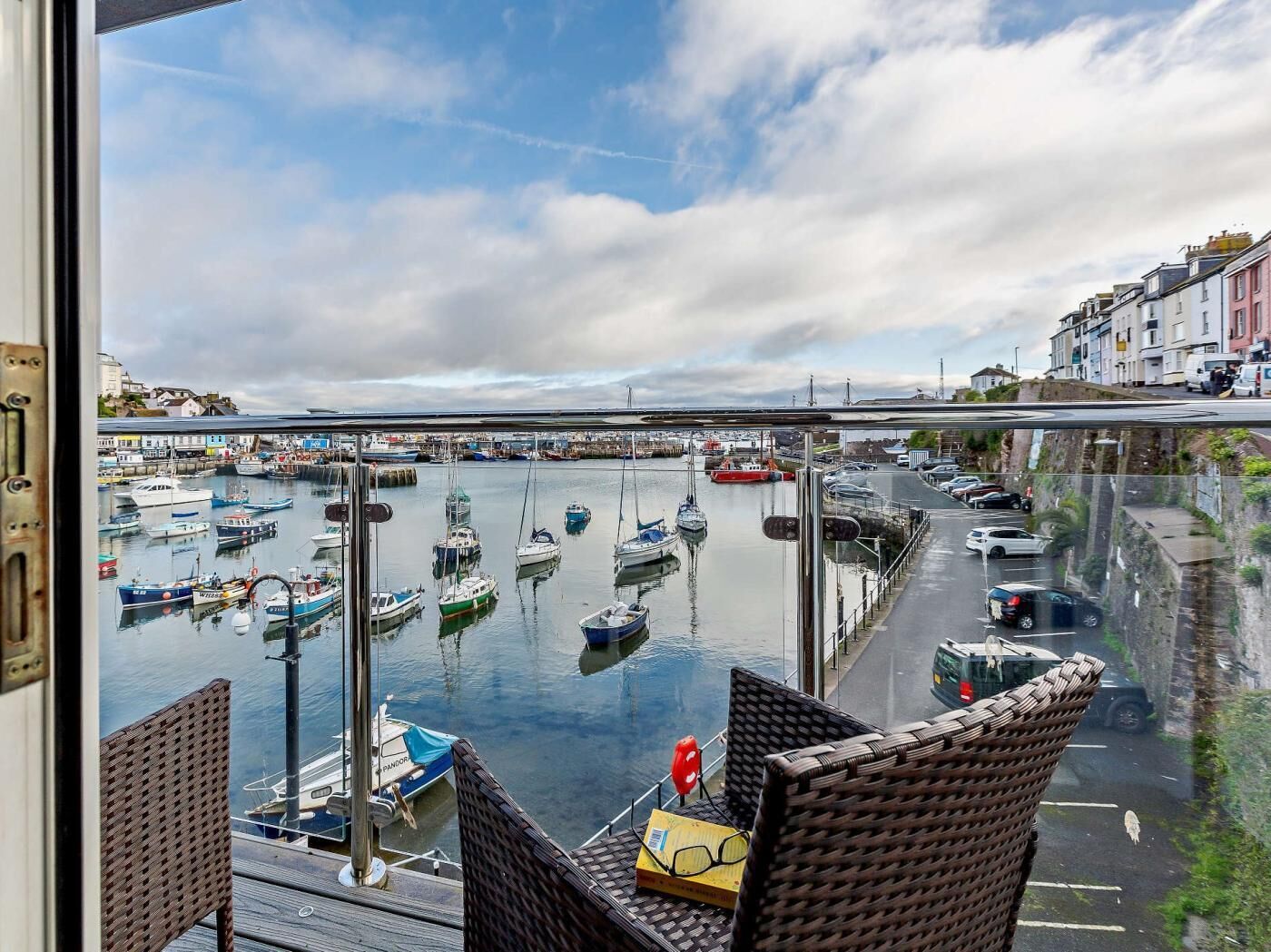 Une vue depuis un balcon donnant sur une marina, avec des bateaux, un pont et des bâtiments en arrière-plan.