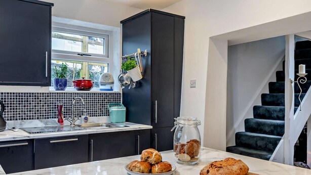 Una cocina moderna con armarios oscuros, encimera de mármol y vista a una escalera.