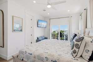 A bedroom with a bed, a ceiling fan, a painting, a door, and a balcony with a railing. - Serenity Seas - All New Luxury Home Across from Beach w/ Heated Pool, Mini Golf (Indian Rocks Beach)