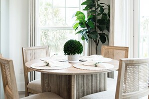 A round dining table with a central potted plant, surrounded by four chairs with woven backs. - Serenity Seas - All New Luxury Home Across from Beach w/ Heated Pool, Mini Golf (Indian Rocks Beach)