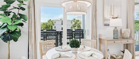 A dining area with a round table, chairs, a hanging light fixture, and a view of the outside.