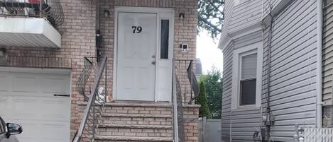 A residential building with a brick facade, a white front door with the number 79, a small porch, and a concrete front steps.