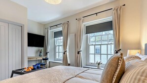 Ein Schlafzimmer mit Bett, Schreibtisch, Fernseher und fensterbelogenen Fenstern.