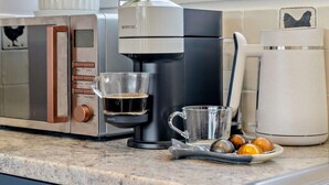 Eine Kaffeemaschine, eine Tasse und ein Teller mit Kaffeebohnen auf einer Küchenarbeitsplatte.