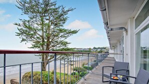 Een balkon met uitzicht op het strand, een boom en een tafel met stoelen.