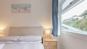 Een slaapkamer met een bed, nachtkastje, lamp en een schilderij aan de muur.
