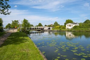 A calm river with a bridge, a grassy path, and a building with columns. - 2 Bed in Gloucester (oc-94228) (Frampton on Severn)