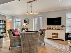 A modern living room with wicker furniture, a flat-screen TV, and a dining area. - 3 Bed in Cottingham (oc-94350) (Raywell)