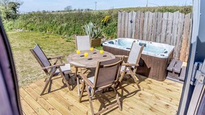 Eine Terrass mit Whirlpool, Holzstühlen und einem Tisch mit Getränken.