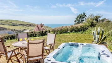A hot tub on a wooden deck with a table and chairs, overlooking a scenic landscape.