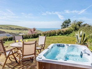 A hot tub on a wooden deck with a table and chairs, overlooking a scenic landscape.