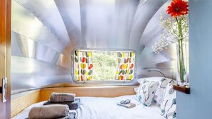 Ein Schlafzimmer mit Fenster, einem Bett, einem Nachttisch mit einer Vase und Blick auf Grün.