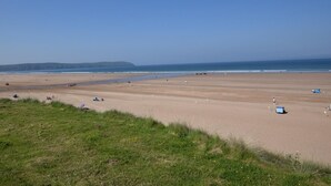 Ein weiter Sandstrand, bewölkter Himmel, Hügel in der Ferne und einige Zelte sowie Personen.