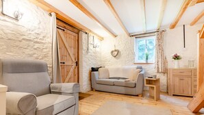 A cozy room with a sofa, armchair, wooden floor, stone wall, and a window with curtains. - 1 Bed in Bideford (oc-folly) (Buckland Brewer)