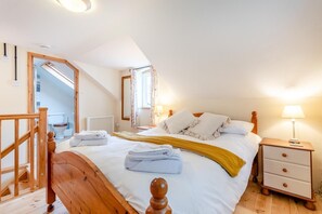 A bedroom with a wooden bed, a nightstand, a lamp, a window with curtains, and a view of the bathroom. - 1 Bed in Bideford (oc-folly) (Buckland Brewer)