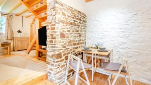 A cozy room with a stone wall, wooden beams, a dining area with a table and chairs, and a television. - 1 Bed in Bideford (oc-folly) (Buckland Brewer)
