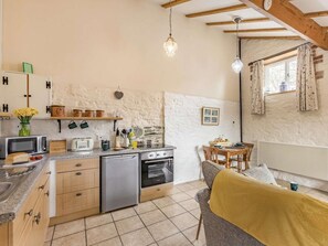 Eine kompakte Küche mit Geschirrspüler, Backofen und Mikrowelle. Es gibt eine Essecke mit Tisch und Stühlen sowie ein Fenster mit Vorhängen.
