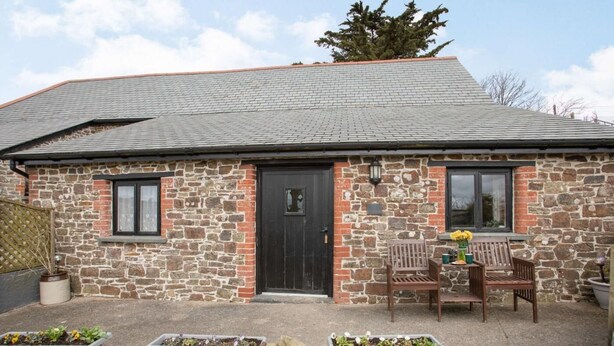 A stone building with a black door, two windows, and a small porch with a bench and potted plants. - 1 Bed in Bideford (oc-pwork) (Buckland Brewer)