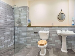 Et moderne badeværelse med en glasbrusekabine, et toilet med træsæde og en konsolvask.