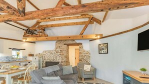 Ein rustikales Interieur mit freiliegenden Holzbalken, einem Kamin aus Stein, einem Essbereich und einer Sitzecke mit Fernseher.