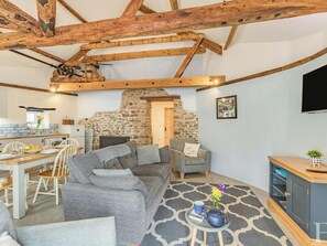 A rustic interior with exposed wooden beams, a stone fireplace, a dining area, and a seating area with a TV. - 2 Bed in Bideford (oc-60765) (Buckland Brewer)