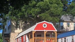A red building with a wooden balcony, a stone wall, and a grassy area in front.