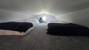 A small, dimly lit attic bedroom with two single beds, a round table, and a fan.
