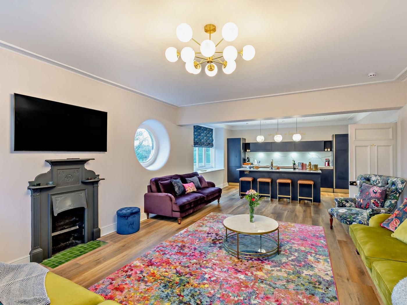 A modern living room with a fireplace, a sofa, a coffee table, and a vibrant rug.