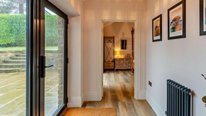 Un couloir avec une porte vitrée donnant sur l’extérieur, un plancher en bois, un lustre et des tableaux encadrés accrochés au mur.