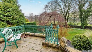 Un banc avec une barrière en métal vert, un chemin de pierre et une vue sur des arbres et un paysage lointain.