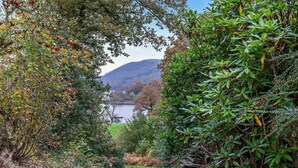 A stone wall with a gate leading to a body of water, surrounded by dense foliage and a hilly landscape in the background. - 2 Bed in Ulverston (oc-91730) (Blawith)
