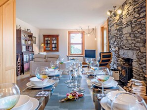 A dining area with a long table set for a meal, a fireplace, and a cozy living room with a sofa and bookshelves. - 2 Bed in Ulverston (oc-91730) (Blawith)