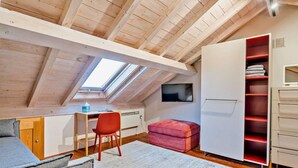 A loft bedroom with a sloped ceiling, a desk, a red chair, a pink ottoman, a white wardrobe, and a TV mounted on the wall. - 2 Bed in Ulverston (oc-91730) (Blawith)