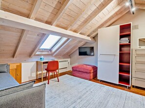 A loft bedroom with a sloped ceiling, a desk, a red chair, a pink ottoman, a white wardrobe, and a TV mounted on the wall. - 2 Bed in Ulverston (oc-91730) (Blawith)