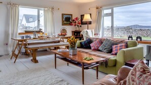 A cozy living room with a dining area, large windows, a view of the sea, and a stone wall. - 4 Bed in Ullapool (oc-ca278) (Achiltibuie)