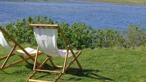 A chair by a lake with a grassy foreground and rocky hills in the background. - 4 Bed in Ullapool (oc-ca278) (Achiltibuie)