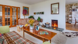 A living room with a sofa, a coffee table, a fireplace, and a bookshelf. - 4 Bed in Ullapool (oc-ca278) (Achiltibuie)